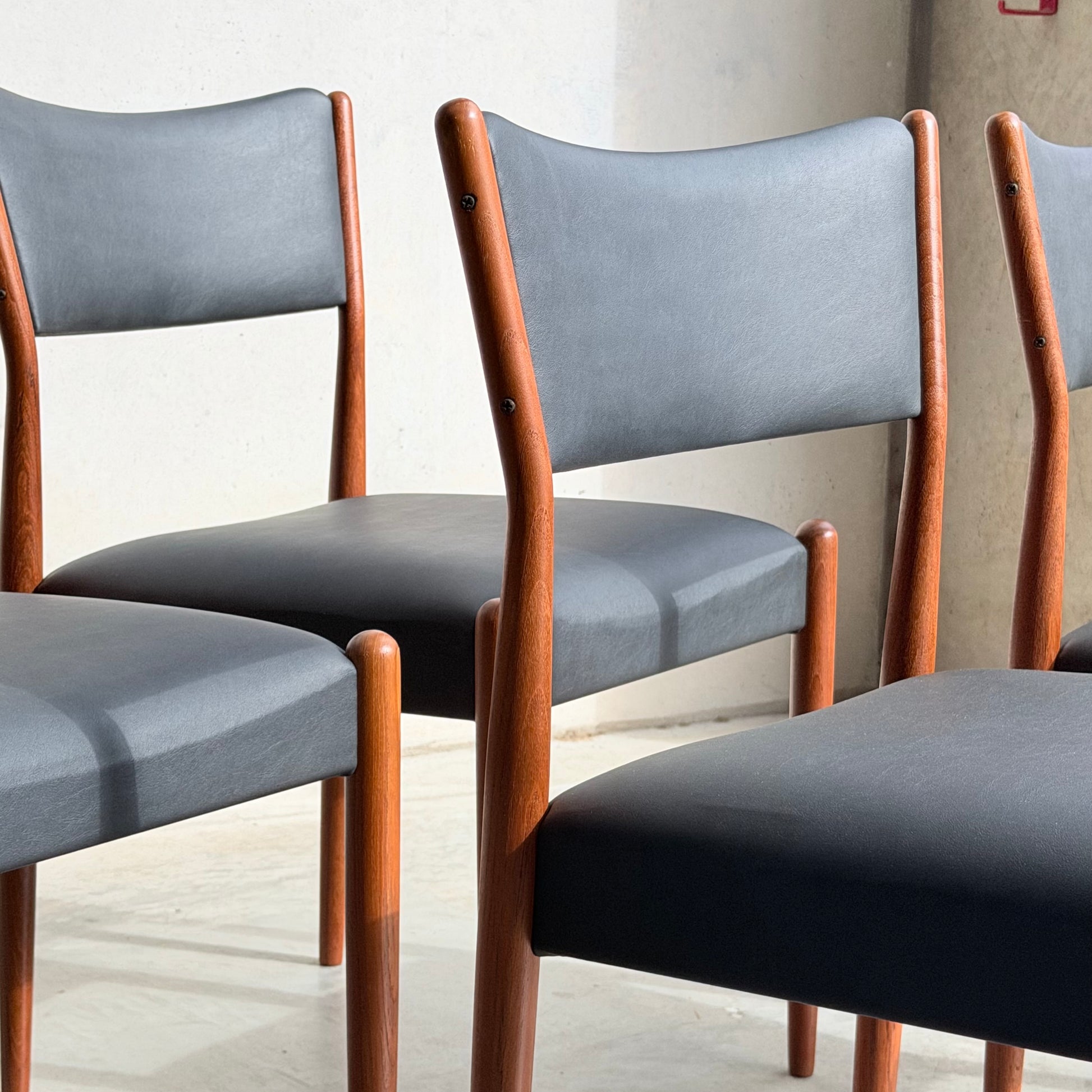Four Parker Number 97 Dining Chairs Set of 4 – Licorice Vinyl (Rediscover) with wooden frames and dark upholstered seats and backs are arranged in sunlight on a light floor, casting soft shadows and evoking classic mid-century elegance.