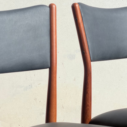 Two Parker Number 97 Dining Chairs in Licorice Vinyl, with curved wooden frames and dark upholstered backs and seats, are set against a light wall. Only the top parts of these mid-century style dining chairs are visible.