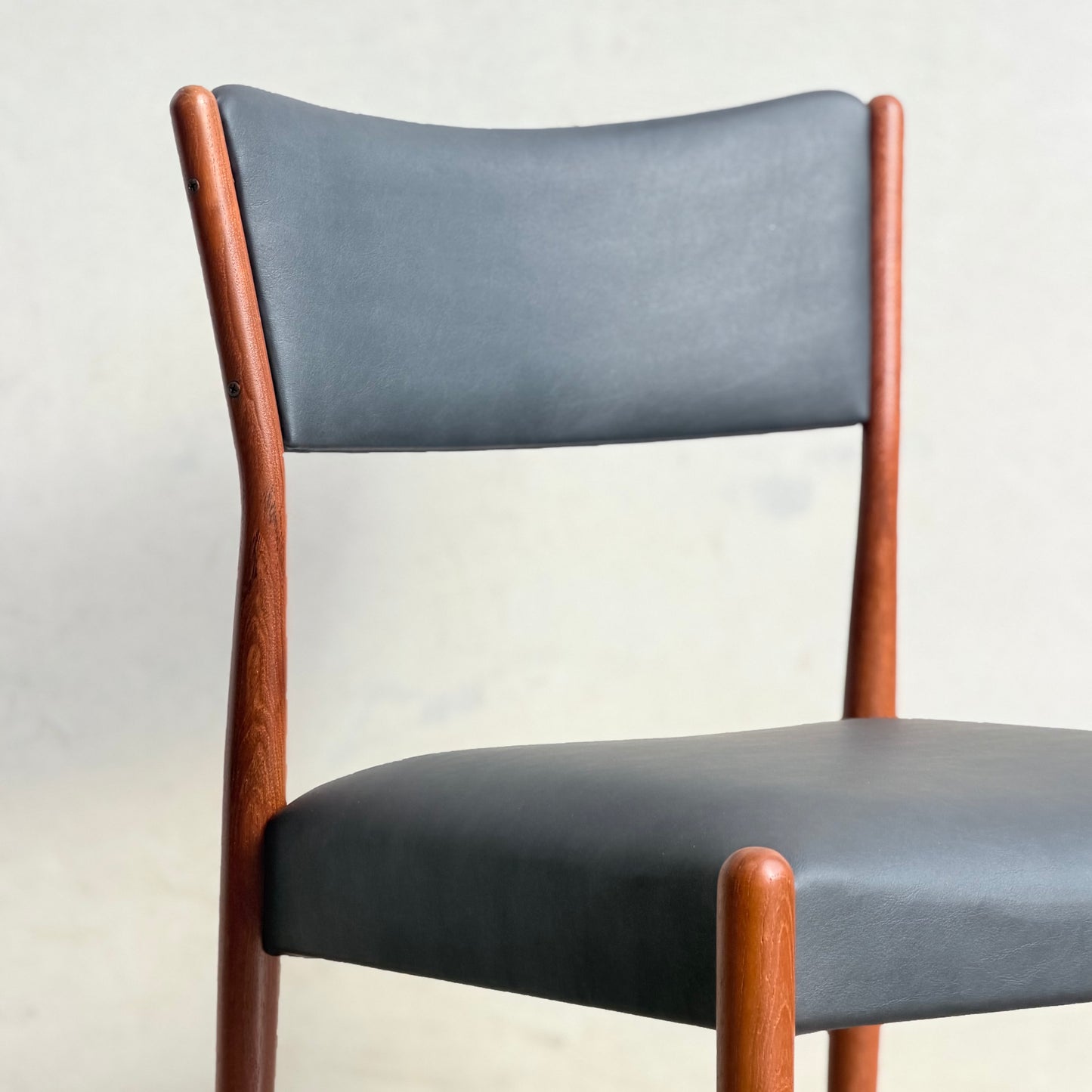 A set of four Parker Number 97 dining chairs features curved wooden frames and padded backrests and seats in licorice vinyl, echoing a modern style, shown against a plain light background.