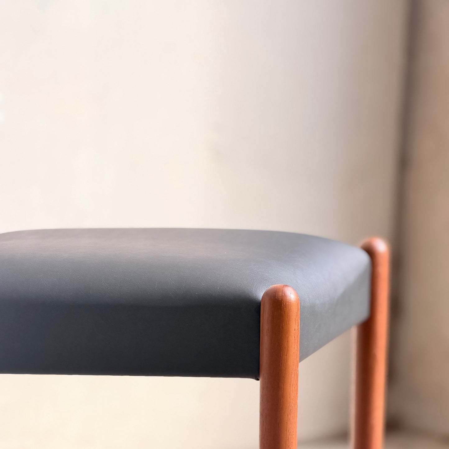 A close-up of Parker Number 97 Dining Chairs Set of 4 – Licorice Vinyl (Rediscover), showcasing their black cushioned seats and wooden legs in a softly lit, neutral setting inspired by mid-century modern design.