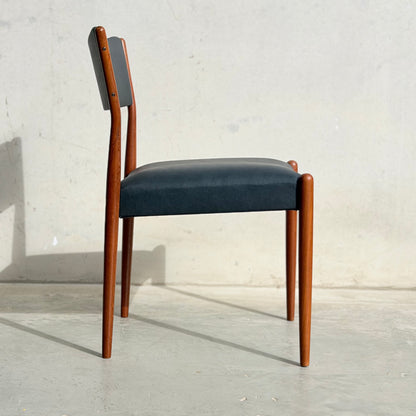 A set of four Parker Number 97 Dining Chairs in Licorice Vinyl features dark cushioned seats and backs with smooth wooden frames, arranged on a light concrete floor against a simple pale wall.
