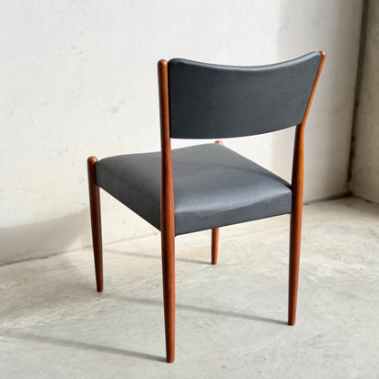 A set of four Parker Number 97 Dining Chairs in licorice vinyl, featuring curved backrests and sleek wooden legs, sits on a light concrete floor against a plain, light-colored wall.