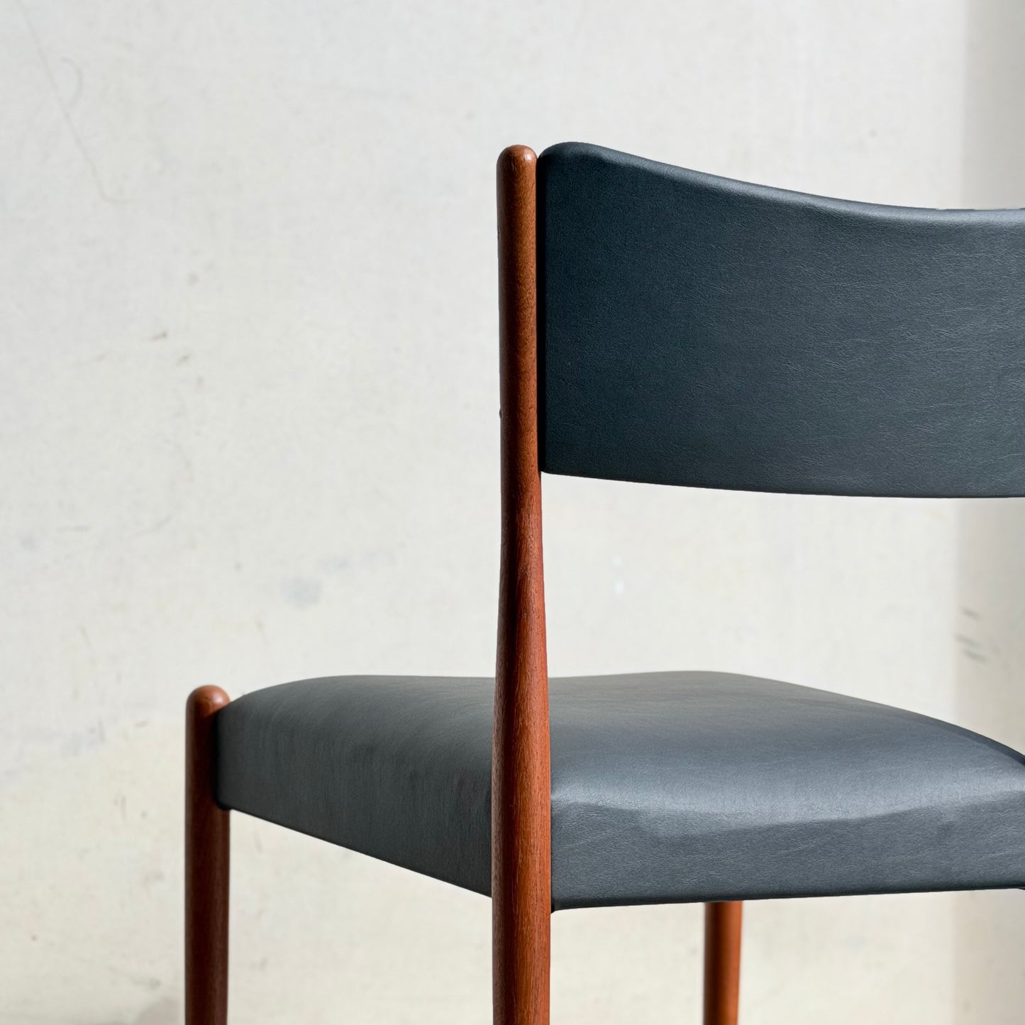 A close-up of the Parker Number 97 Dining Chairs Set of 4 in Licorice Vinyl, featuring a dark, curved backrest and seat with slender wooden legs, showcased against a plain, light-colored wall.