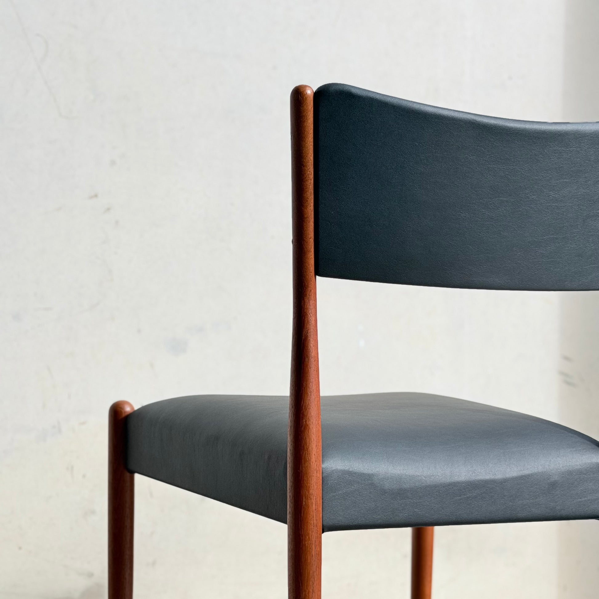 A close-up of the Parker Number 97 Dining Chairs Set of 4 in Licorice Vinyl, featuring a dark, curved backrest and seat with slender wooden legs, showcased against a plain, light-colored wall.