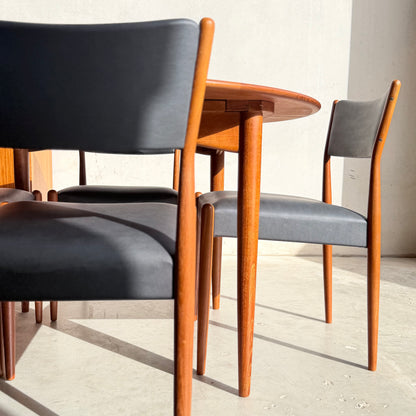 Sunlight highlights a set of Parker Number 97 Dining Chairs Set of 4 – Licorice Vinyl (Rediscover) around a round wooden table, casting graceful shadows on the light floor and wall.