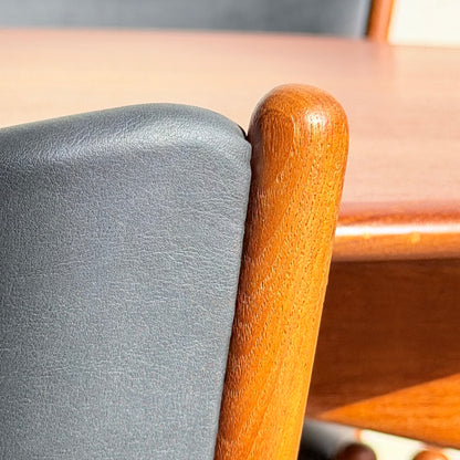 Close-up of a Parker Number 97 Dining Chairs Set of 4 – Licorice Vinyl (Rediscover) backrest against a wooden dining table. The rounded frame and sunlight highlight the rich wood grain and classic mid-century modern style.