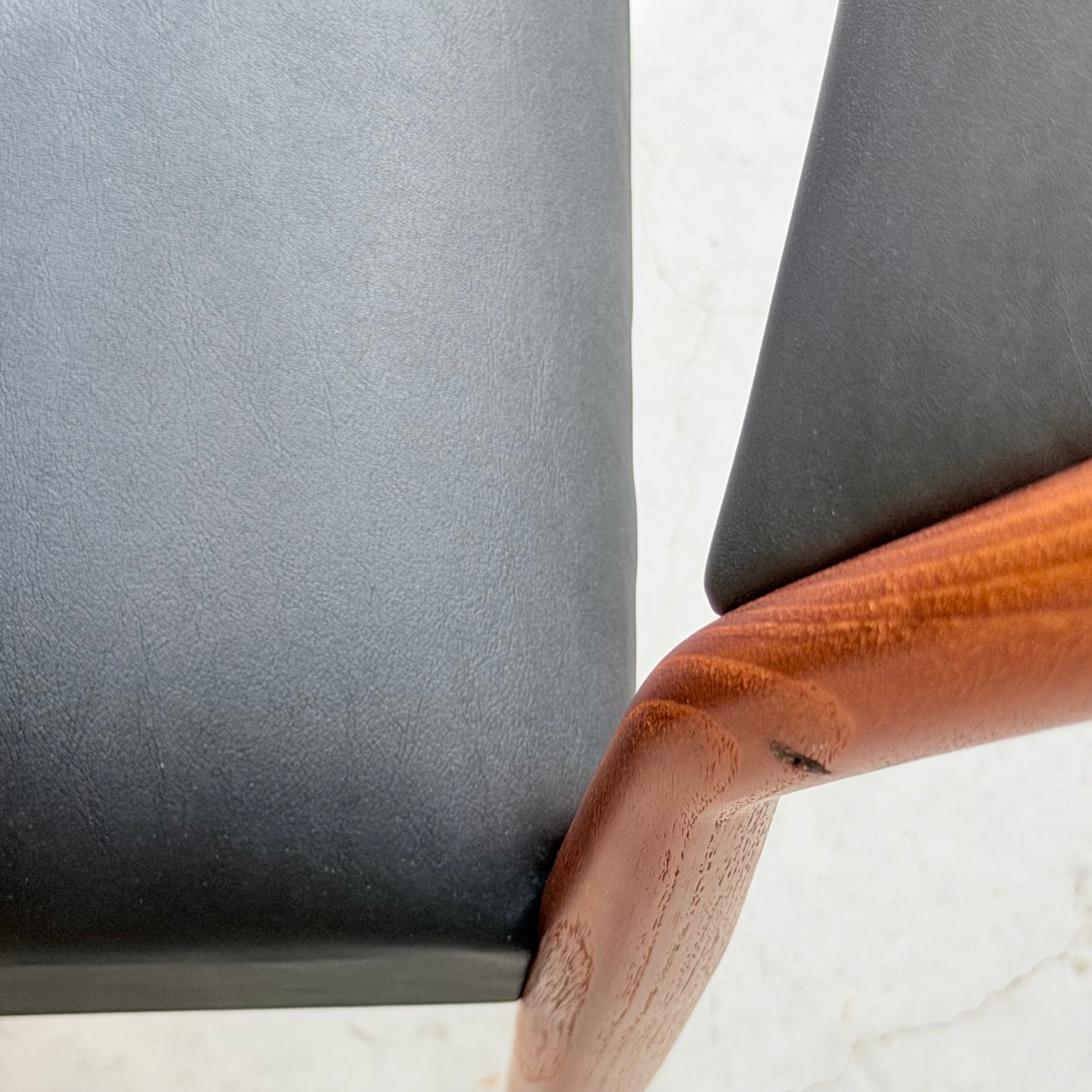 Close-up of the Parker Number 97 Dining Chairs Set of 4 – Licorice Vinyl, displaying a curved wooden frame and sleek black vinyl seat against a light textured background.