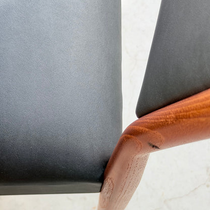 Close-up of the Parker Number 97 Dining Chairs Set of 4 – Licorice Vinyl, displaying a curved wooden frame and sleek black vinyl seat against a light textured background.