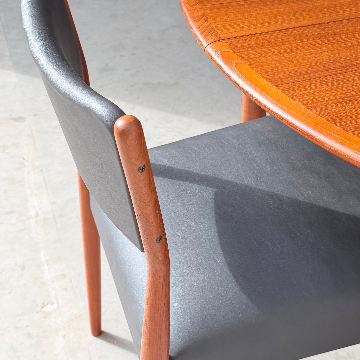 A close-up of the Parker Number 97 Dining Chairs Set of 4 – Licorice Vinyl (Rediscover) beside a round wooden table, displayed on a light floor in natural sunlight.