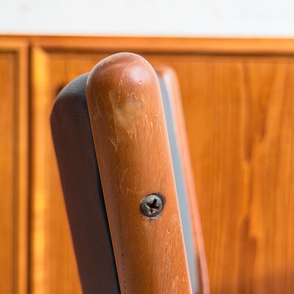 Close-up of the top corner of a Parker Number 97 Dining Chairs Set of 4 – Licorice Vinyl (Rediscover) backrest, showing scratches and a screw, with a wooden paneled wall in the background.