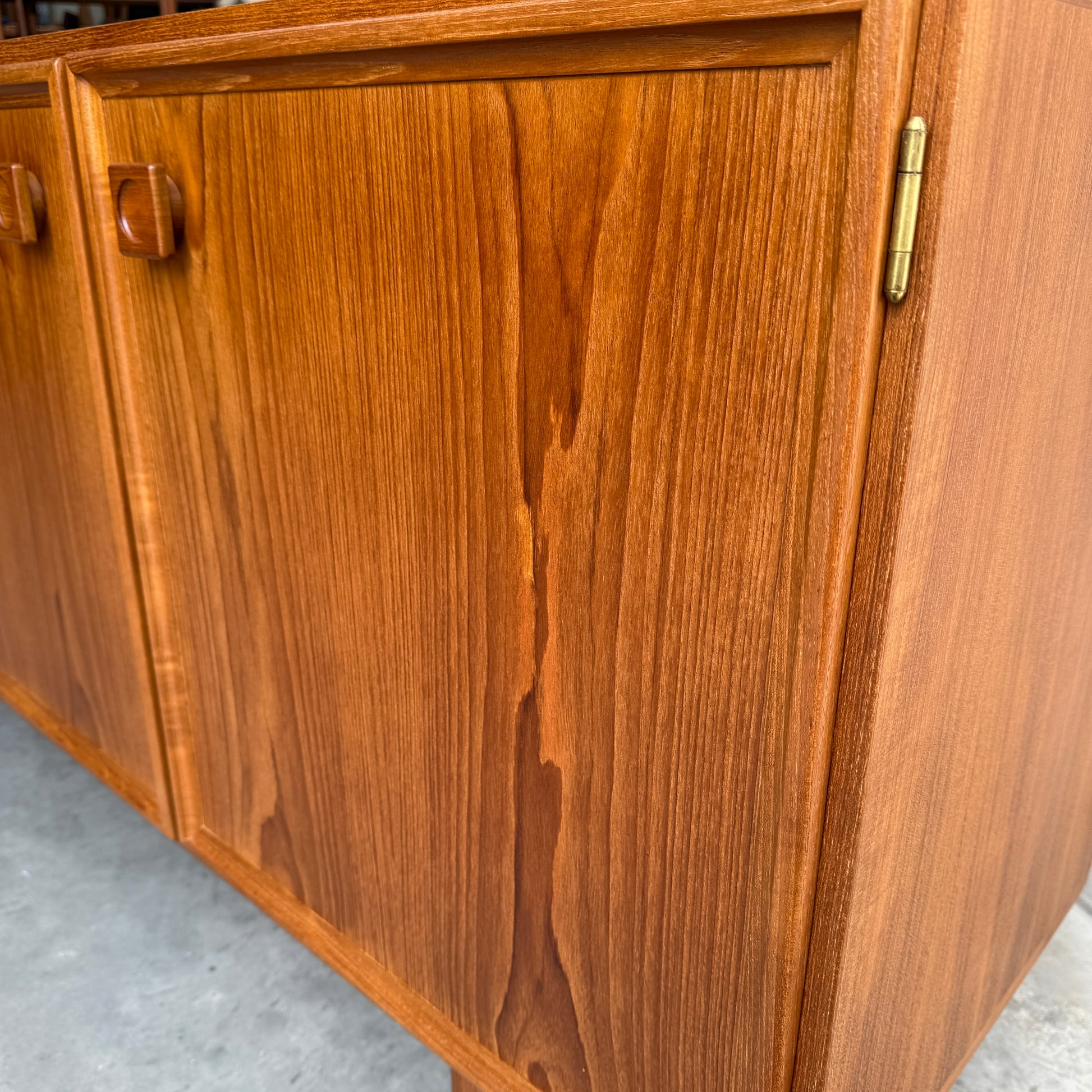 Close-up of the Iconic Parker Teak 4-Door Sideboard – a restored mid-century modern piece with natural finish, tapered legs, visible wood grain, square handles, and brass hinges showcasing Australian craftsmanship.