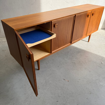 The Iconic Parker Teak 4-Door Sideboard – Restored Mid Century Modern with Tapered Legs (Rediscover) stands on four legs atop a bare concrete floor, showcasing Australian craftsmanship and featuring both closed and open storage.