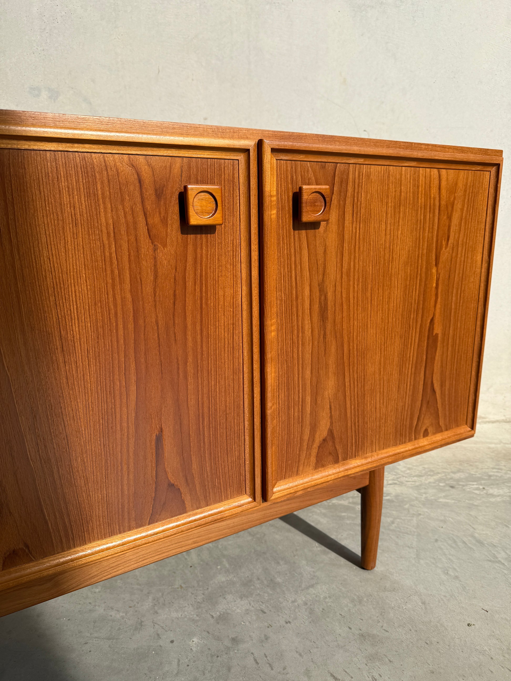 A close-up of the Iconic Parker Teak 4-Door Sideboard – a restored mid century modern piece with tapered legs – showcases Australian craftsmanship, set on concrete against a plain light wall.