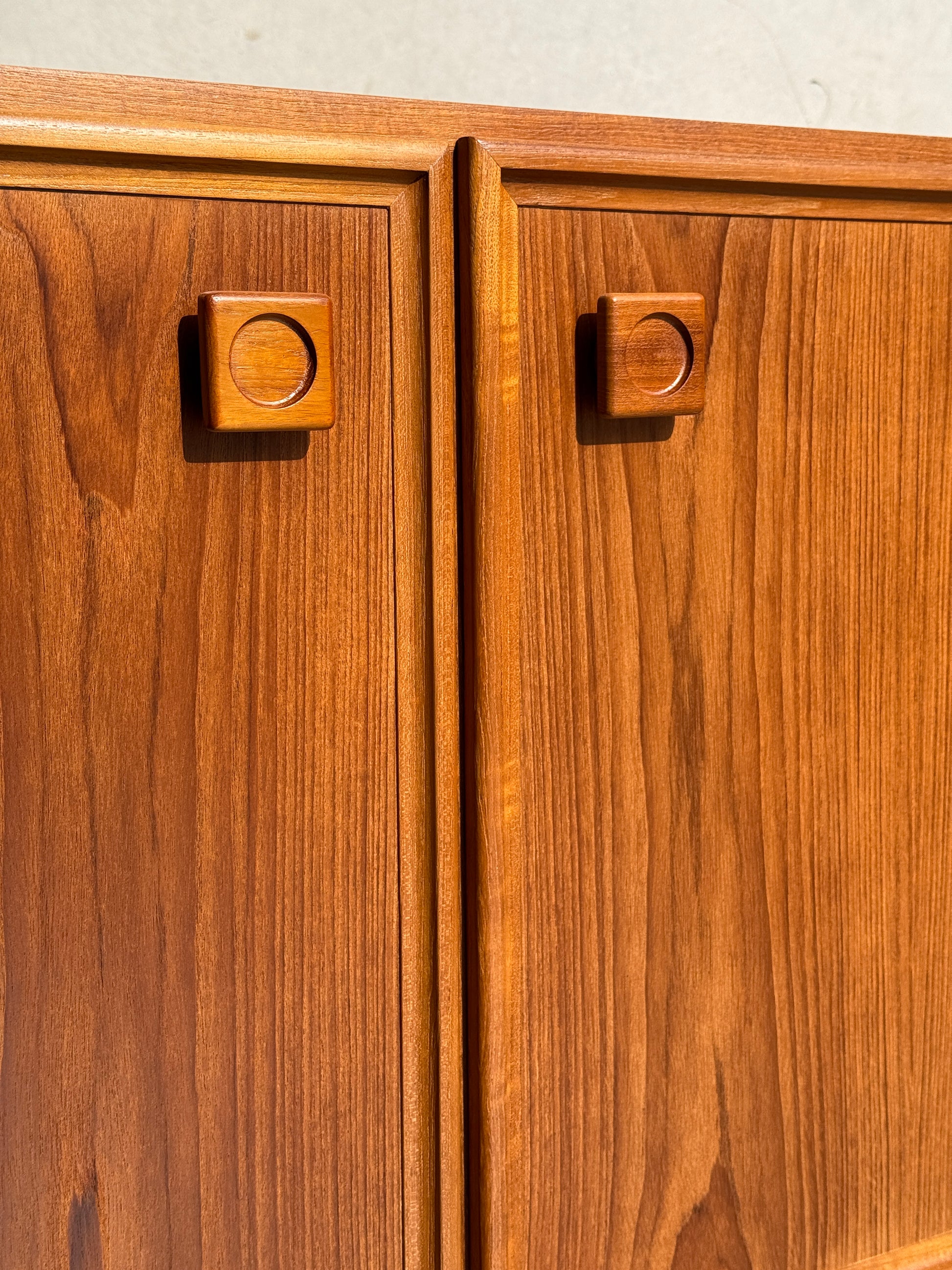 Close-up of the Iconic Parker Teak 4-Door Sideboard’s cabinet doors with square handles, highlighting natural wood grain and warm tones in bright light—a restored mid-century modern piece with tapered legs from Australia.