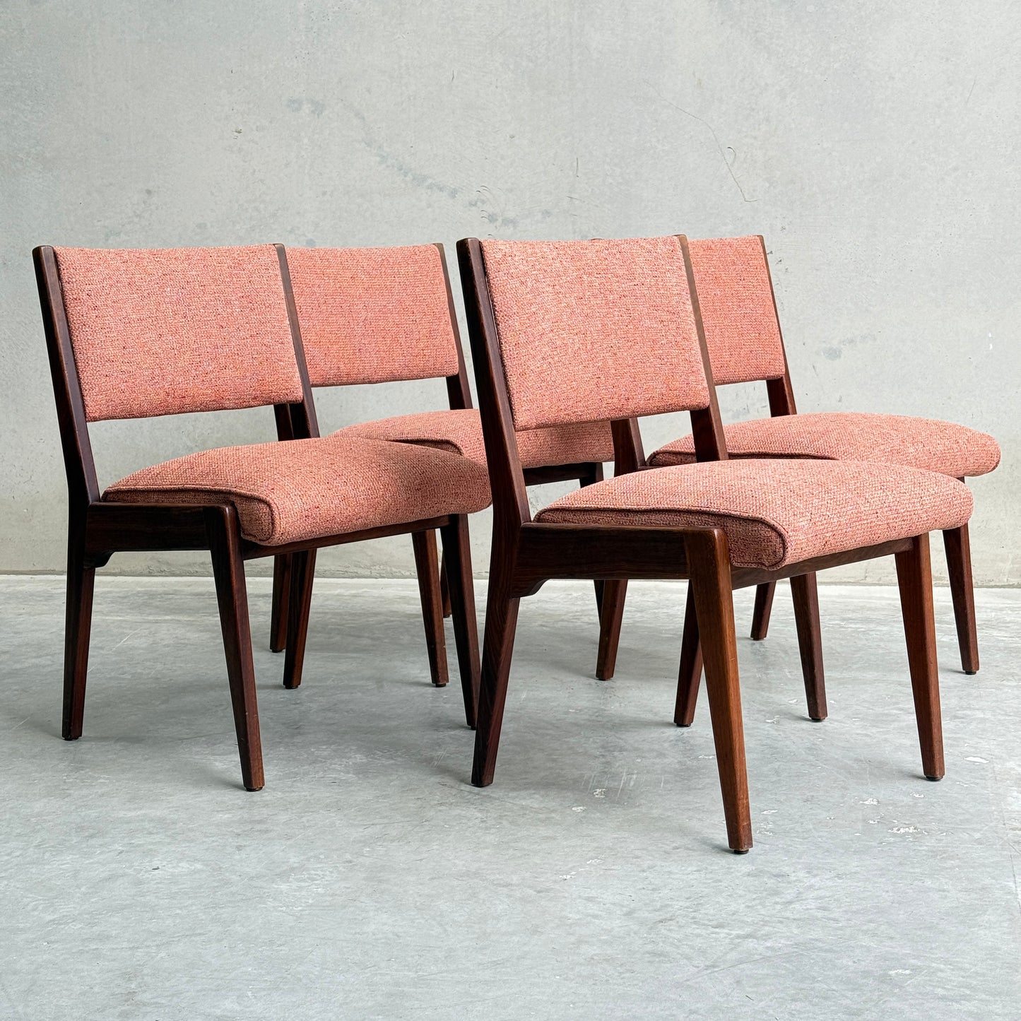 A collectable set of 4 Vintage MCM Jens Risom Chairs features pink upholstered seats and backs, arranged in two rows against a light gray concrete wall, showcasing Scandinavian-inspired mid-century modern design with angled legs.