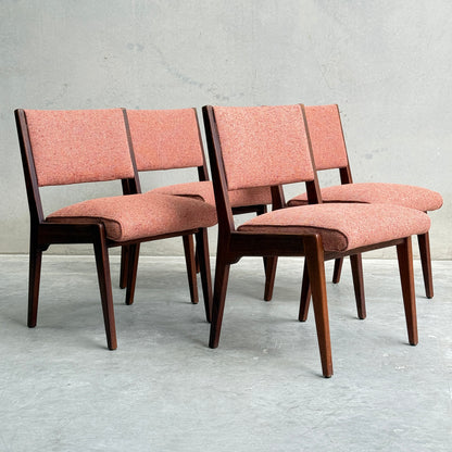 A collectable set of 4 Vintage MCM Jens Risom Chairs features pink upholstered seats and backs, arranged in two rows against a light gray concrete wall, showcasing Scandinavian-inspired mid-century modern design with angled legs.