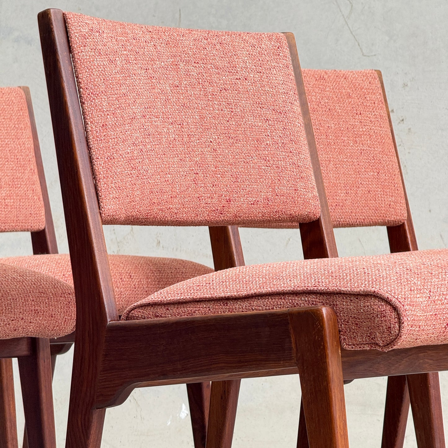 A collectable set of four Vintage MCM Jens Risom Chairs with angled legs and pink upholstery, inspired by Scandinavian design, are placed in front of a plain light gray wall.