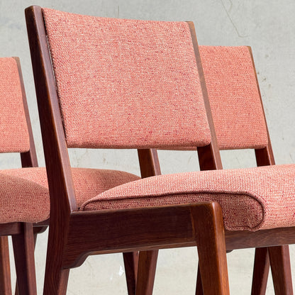 A collectable set of four Vintage MCM Jens Risom Chairs with angled legs and pink upholstery, inspired by Scandinavian design, are placed in front of a plain light gray wall.