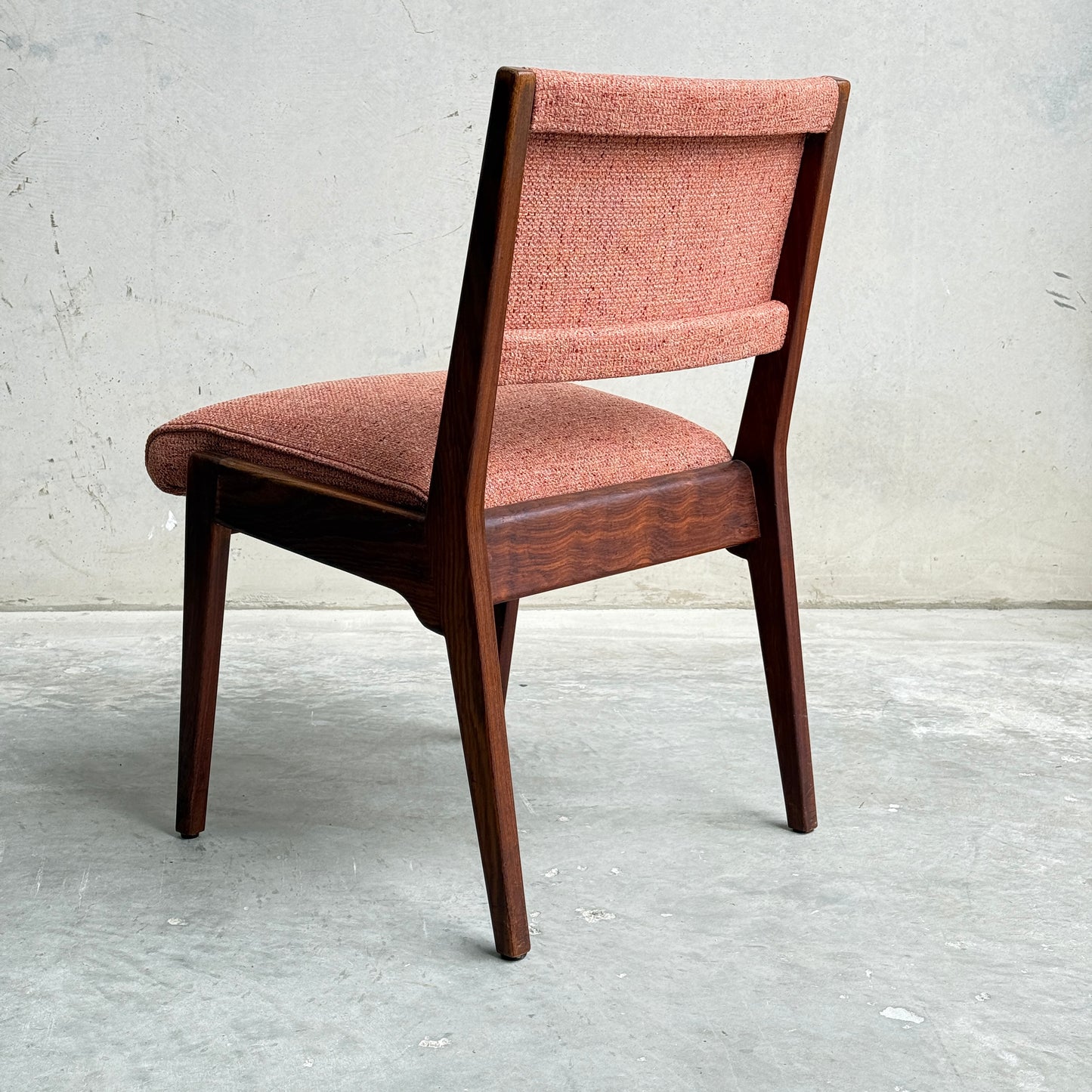 A collectable set of 4 vintage MCM Jens Risom chairs, each with angled legs and textured pinkish-red upholstery, sits on a concrete floor against a light wall, viewed from behind to showcase classic Scandinavian design influences.