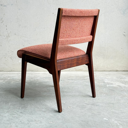 A collectable set of 4 vintage MCM Jens Risom chairs, each with angled legs and textured pinkish-red upholstery, sits on a concrete floor against a light wall, viewed from behind to showcase classic Scandinavian design influences.