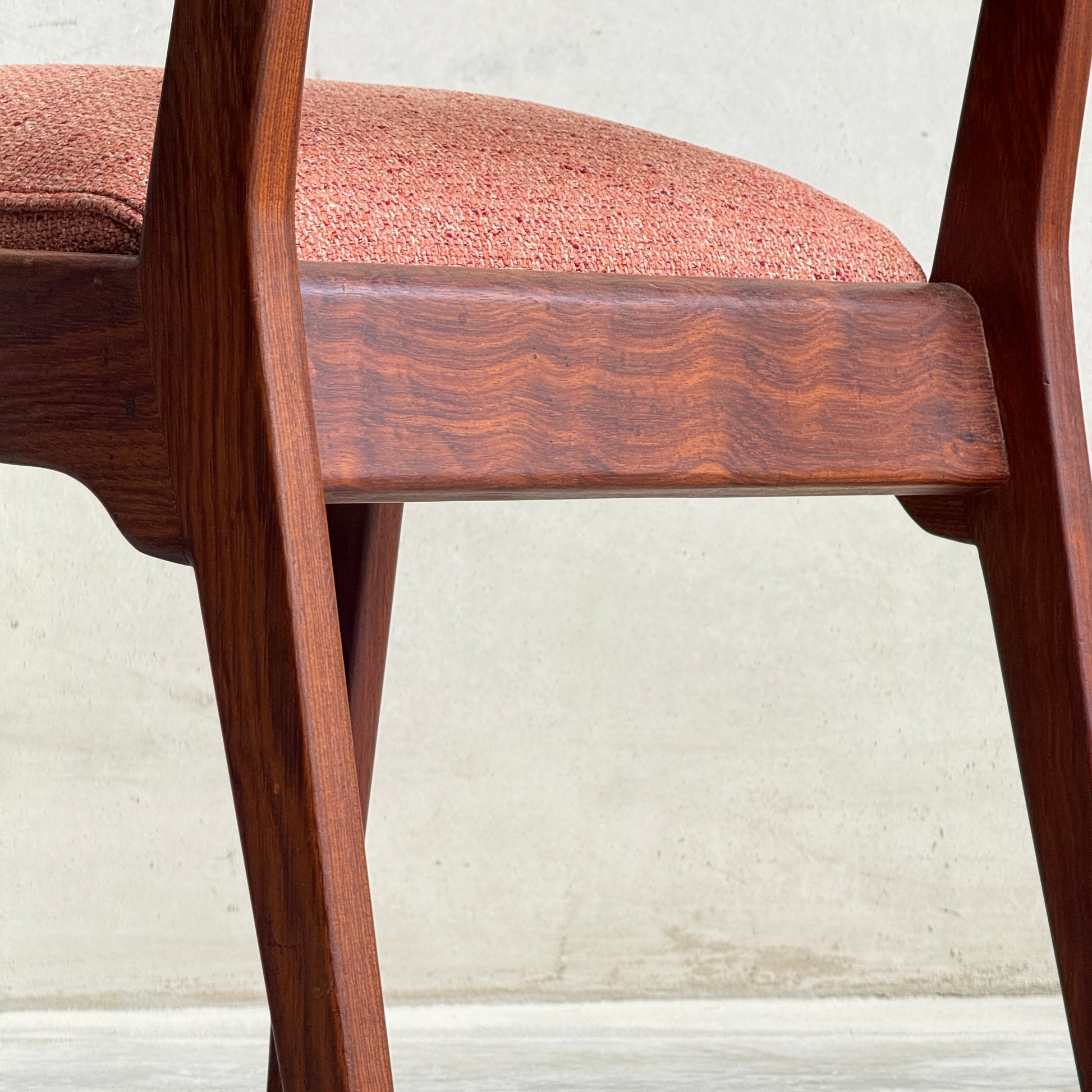 Close-up of a Vintage MCM Jens Risom Chair from a collectable set of 4, featuring angled wooden legs and a pink textured upholstered seat, inspired by classic mid-century modern design, shown against a light wall and concrete floor.