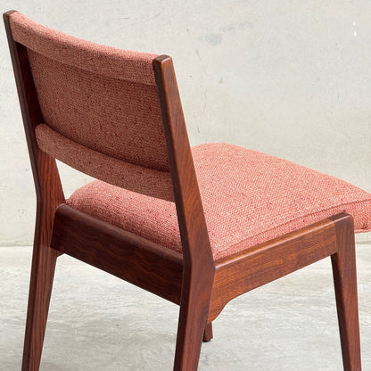 A collectable set of 4 vintage MCM Jens Risom chairs featuring angled wooden legs and reddish textured fabric seats and backrests, showcased against a plain light background.
