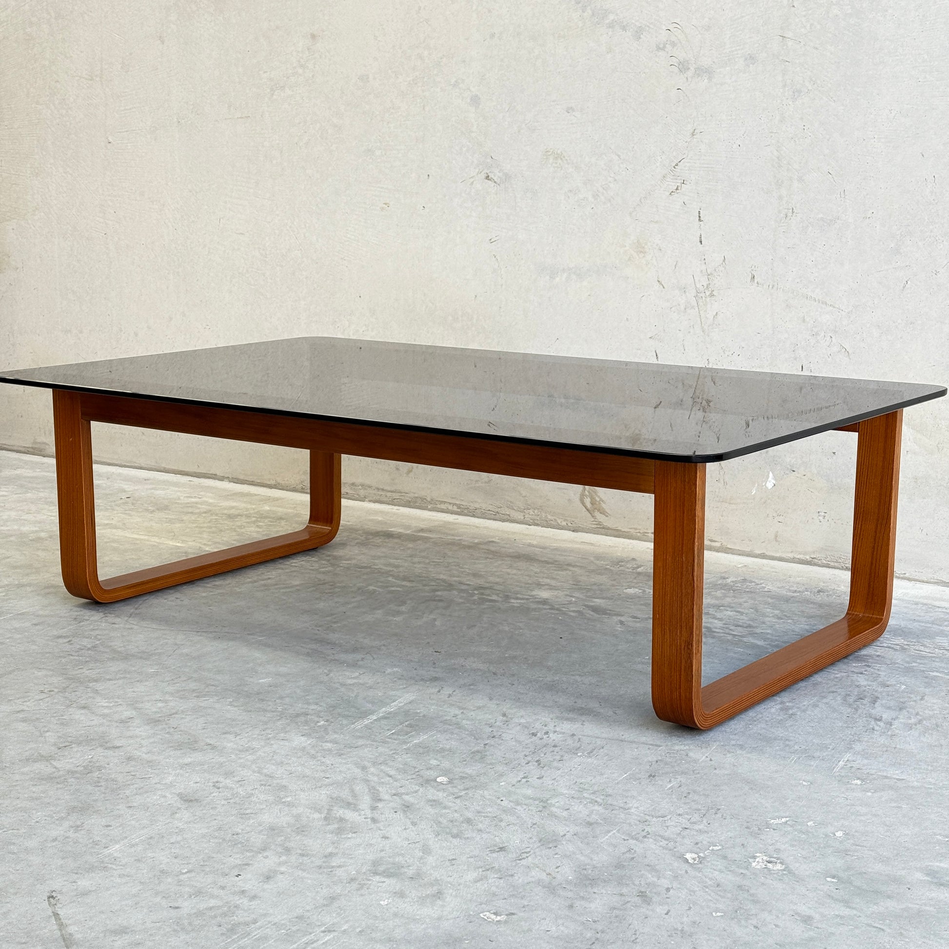 The Tessa T4 - Large Coffee Table (Revive) features a modern minimalist design with a rectangular, dark-tinted glass top and wooden legs in a seamless loop style, perfect for contemporary spaces.