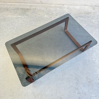 The Tessa T4 - Large Coffee Table (Revive) features a minimalist wooden frame and glass top, set on a concrete floor. Viewed from above, its glass surface reflects light, showcasing the table’s legs and sleek design below.