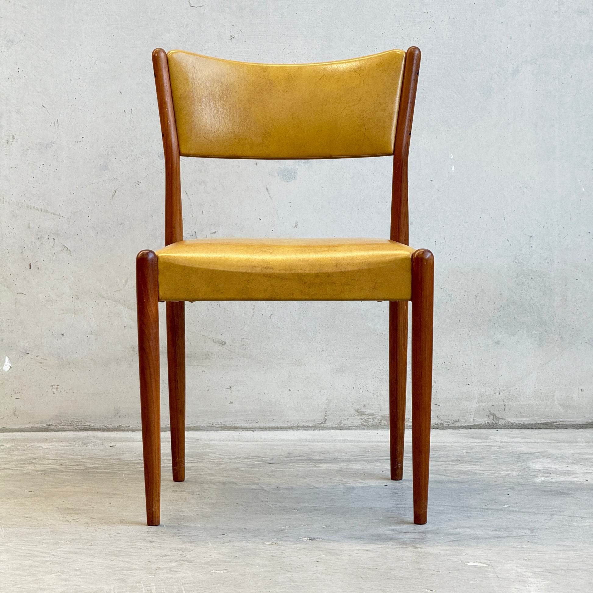 A set of six Parker Number 97 Dining Chairs in original mustard vinyl upholstery is displayed against a plain light gray concrete wall and floor.