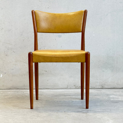 A set of six Parker Number 97 Dining Chairs in original mustard vinyl upholstery is displayed against a plain light gray concrete wall and floor.