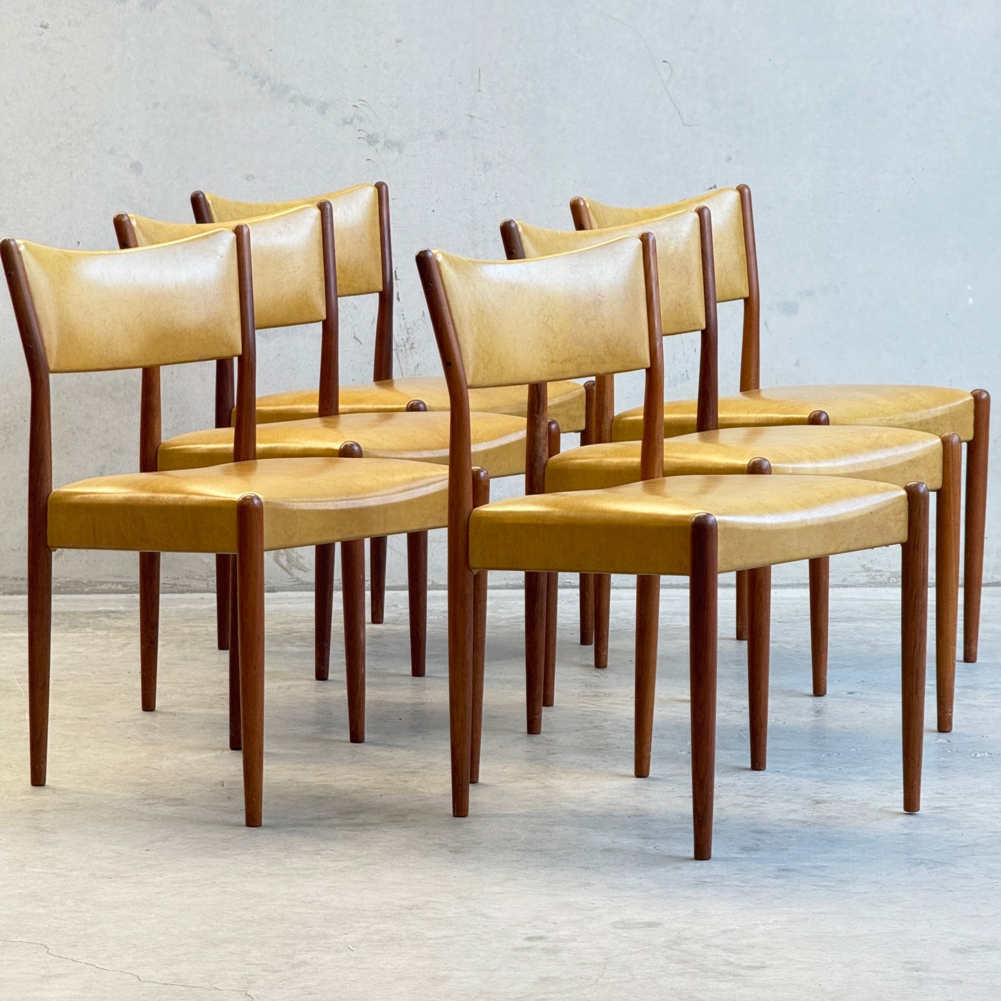 A set of six Parker Number 97 Dining Chairs in original mustard vinyl is arranged in two rows on a light floor, displayed against a plain gray wall.