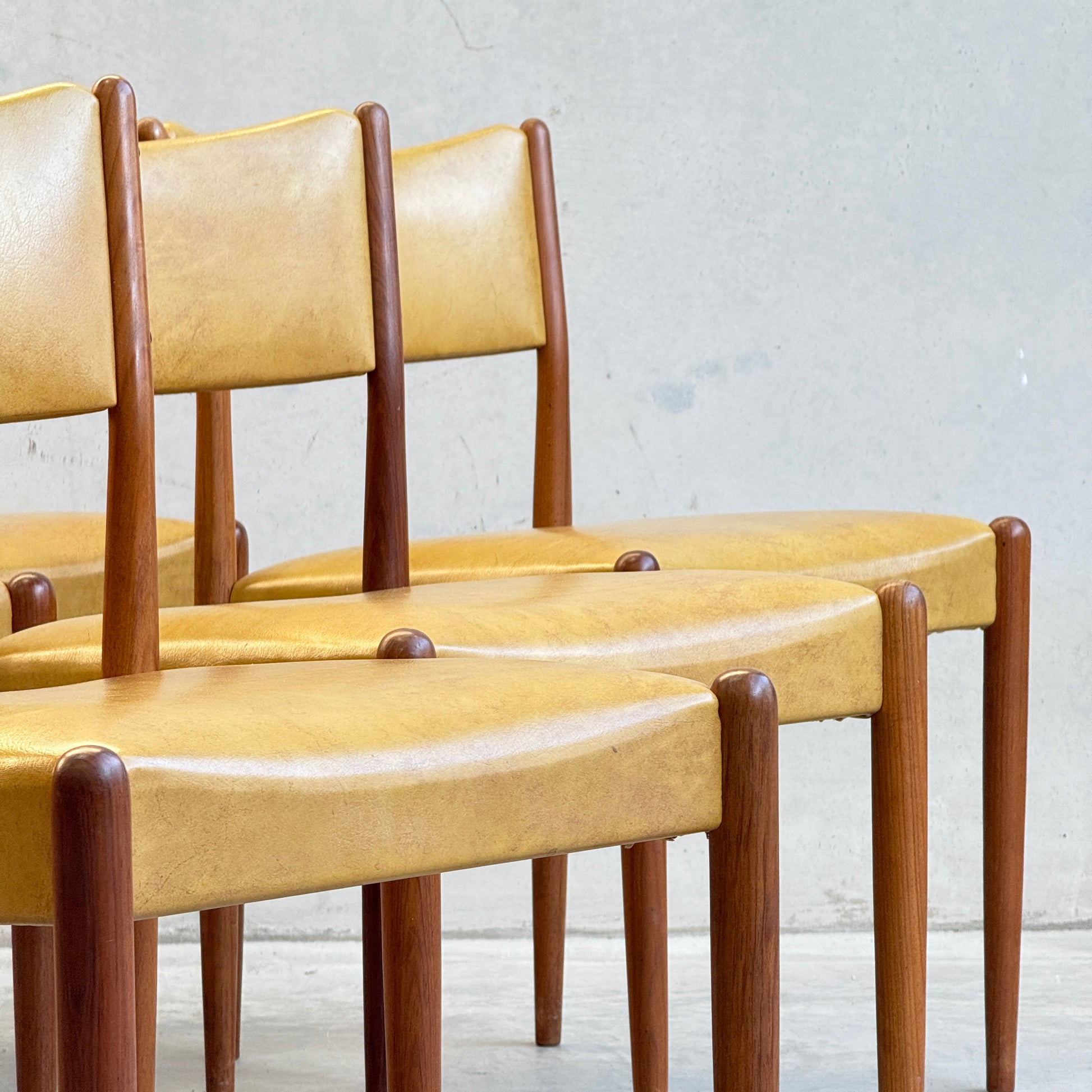 A close-up of six Parker Number 97 Dining Chairs in original mustard vinyl, arranged in a row against a light wall for an authentic mid-century modern aesthetic.