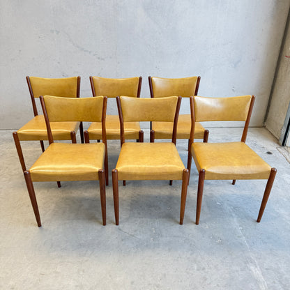 Six Parker Number 97 Dining Chairs Set of 6 – Original Mustard Vinyl are arranged in two rows against a plain, light-colored wall on a concrete floor, highlighting their classic mid-century modern style.