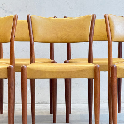 A set of six Parker Number 97 Dining Chairs with original mustard vinyl upholstery, arranged together against a light grey wall, embodying classic mid-century modern style.