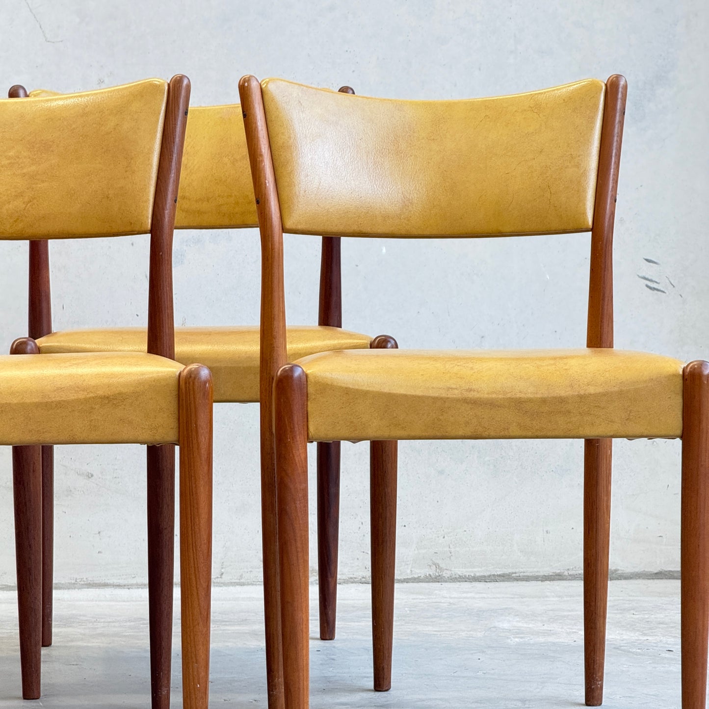 A set of six Parker Number 97 dining chairs with mid-century modern wooden frames and original mustard vinyl upholstery is displayed side by side against a plain, light-colored wall.