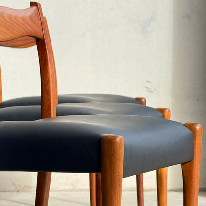 A fully restored set of 6 Fler 64 dining chairs in liquorice vinyl is arranged in a row against a light-colored wall, with sunlight casting soft shadows.
