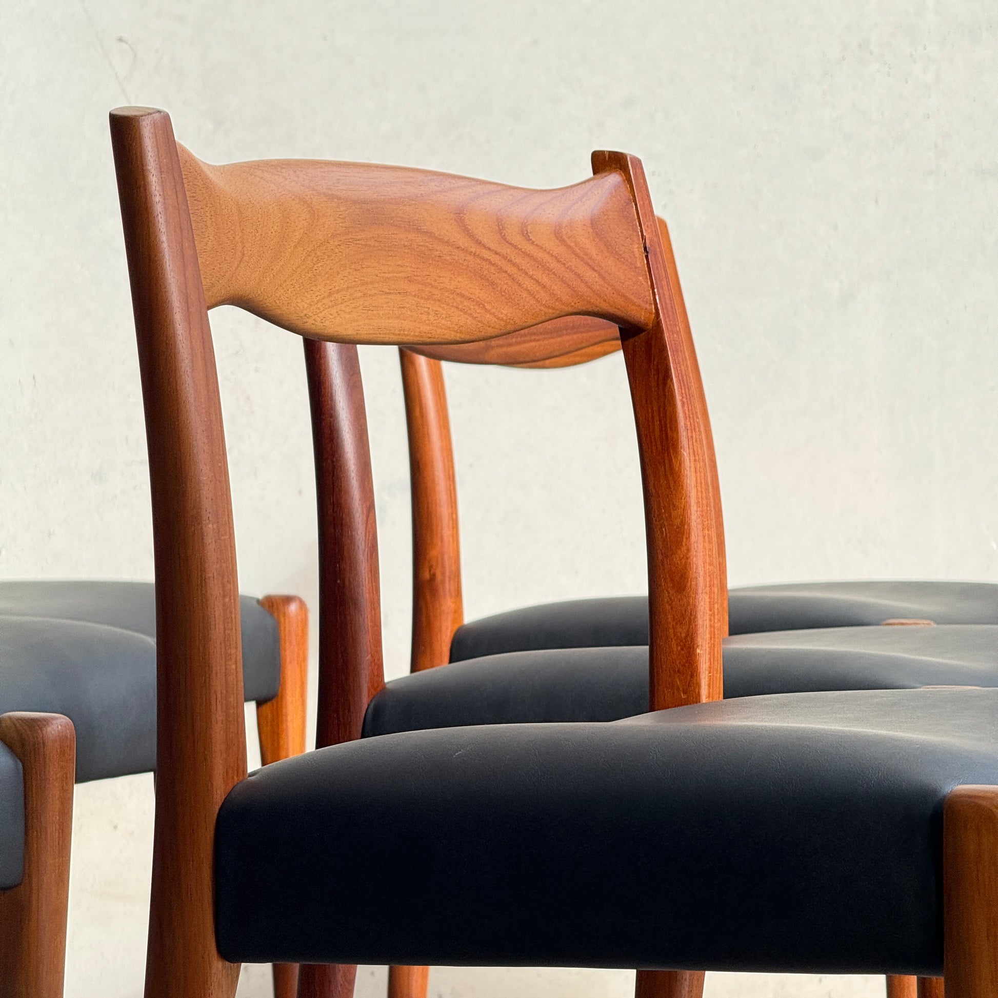 A close-up of a fully restored set of 6 Fler 64 dining chairs with curved backs and liquorice vinyl seats, arranged in a row against a plain light-colored background.