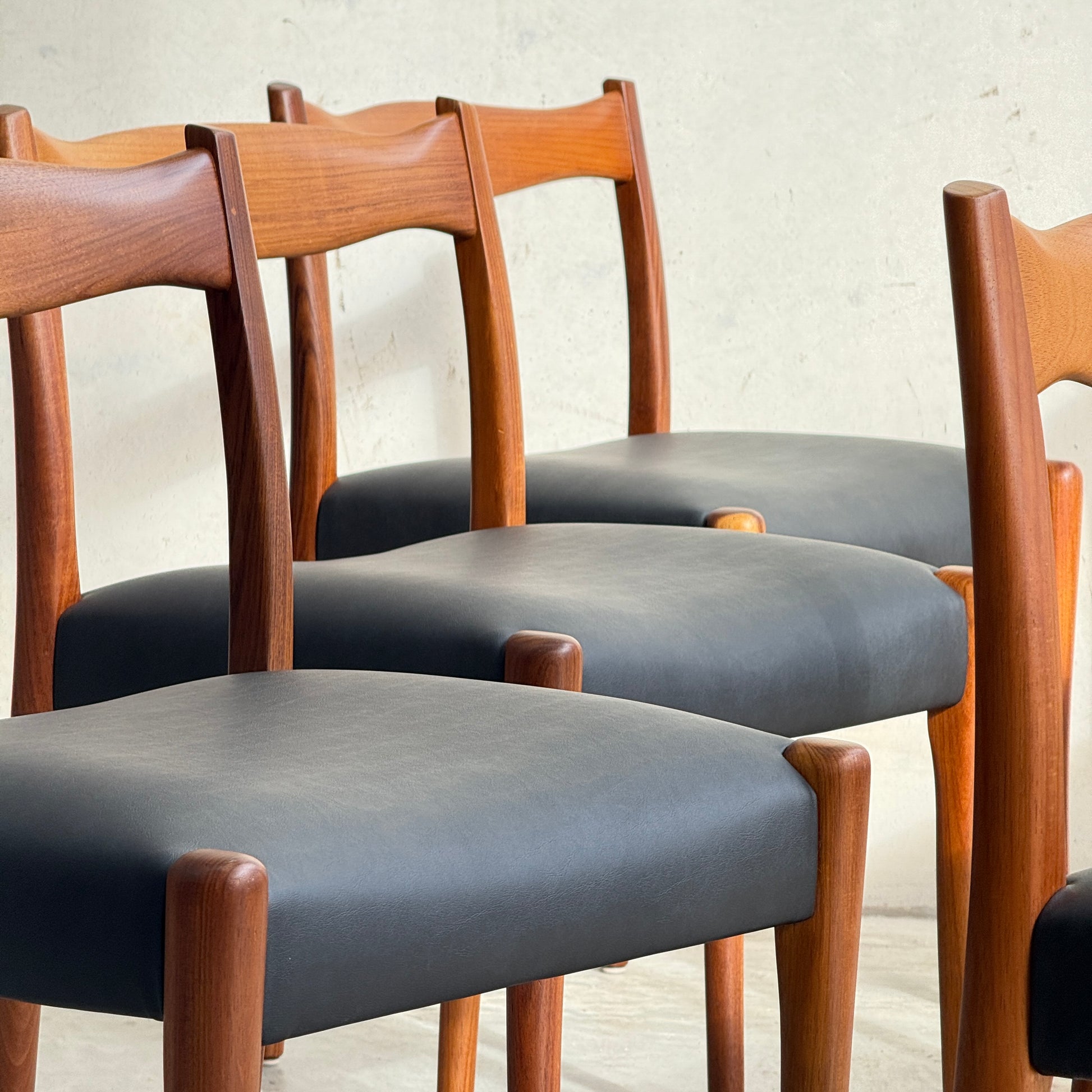 A fully restored set of 6 Fler 64 dining chairs in liquorice vinyl features curved backs and black cushioned seats, arranged together against a light wall for a timeless mid-century modern look.