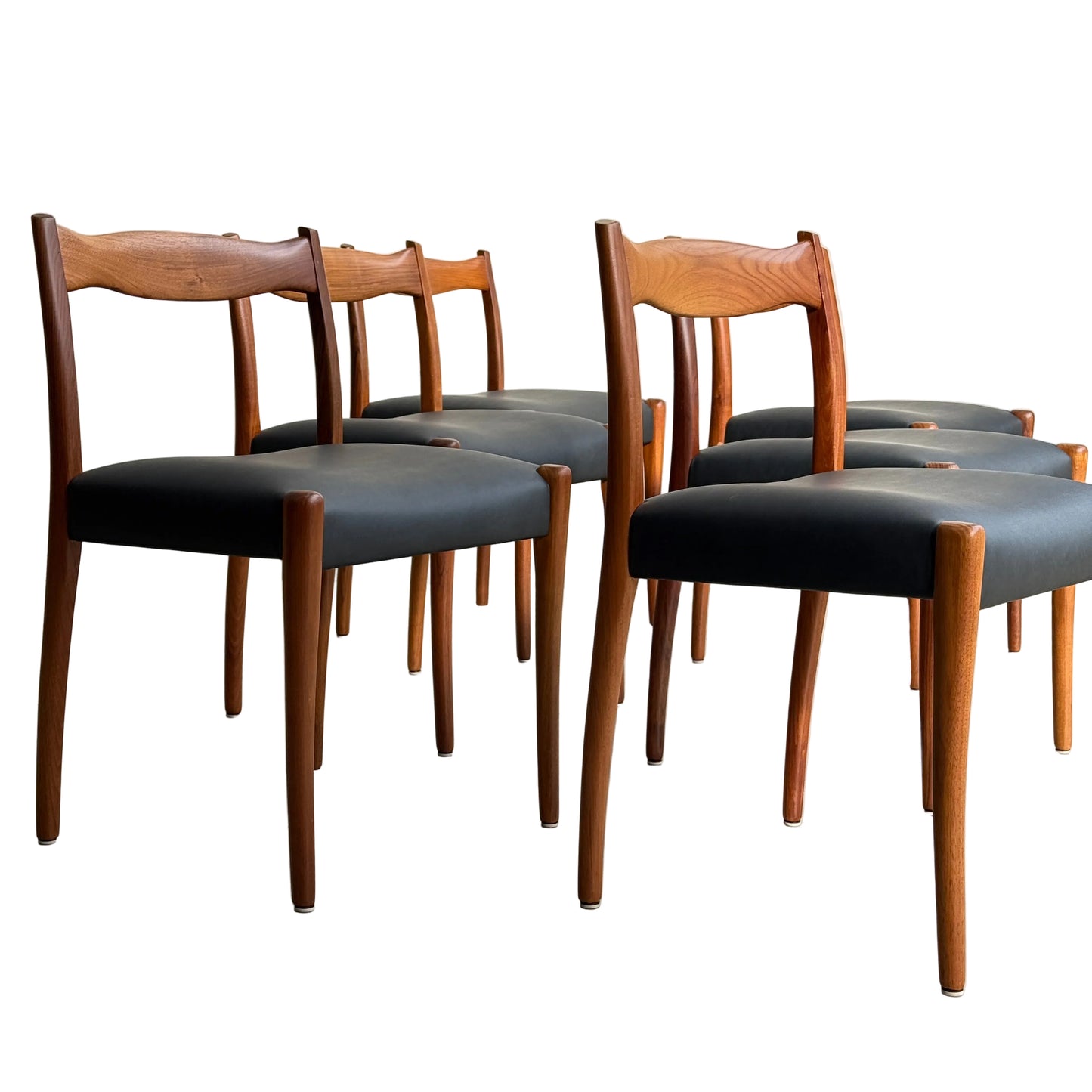A fully restored set of six Fler 64 dining chairs in liquorice vinyl is arranged on a light floor against a plain wall, showcasing classic mid-century modern style.