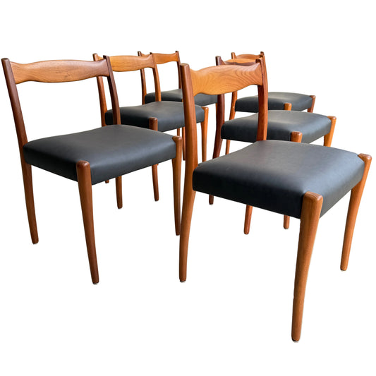 A fully restored set of 6 Fler 64 dining chairs in liquorice vinyl with wooden frames, clean lines, and slightly curved backrests is arranged on a light concrete floor against a neutral wall.