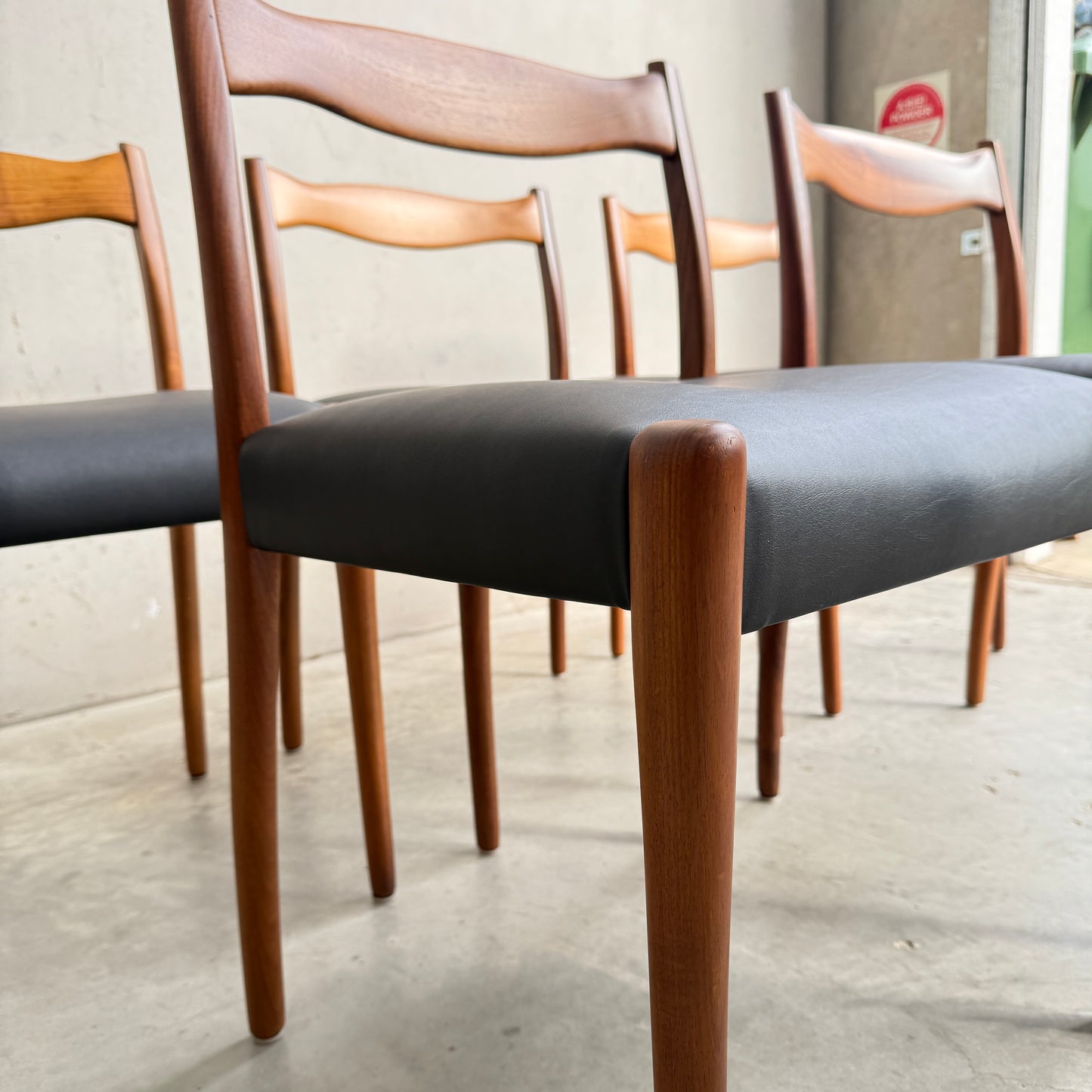 Close-up of the Fully Restored Set of 6 Fler 64 Dining Chairs – Liquorice Vinyl by Rediscover, featuring curved backs and black upholstery, arranged on a concrete floor in a minimalist, mid-century modern indoor space.