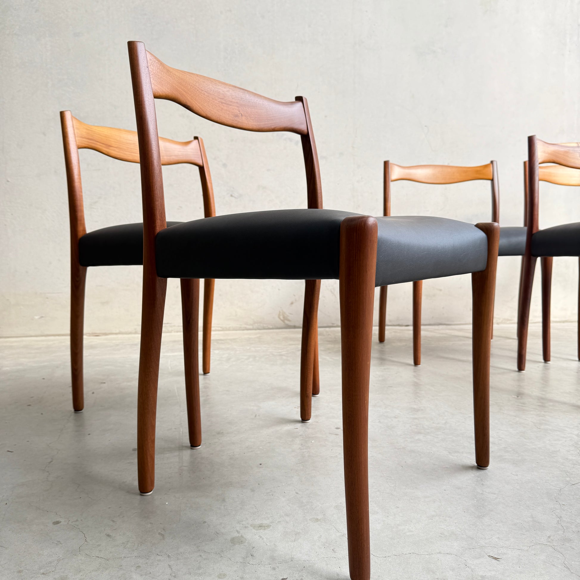 A fully restored set of 6 Fler 64 dining chairs in liquorice vinyl is arranged on a smooth, light-colored concrete floor against a plain, light-colored wall.