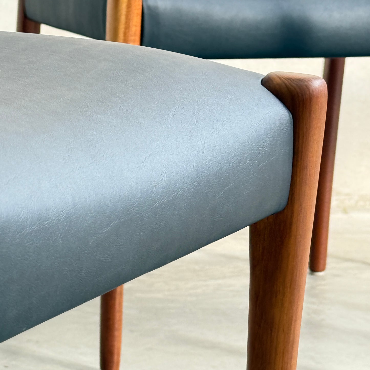 Close-up of two Fully Restored Fler 64 Dining Chairs in liquorice vinyl with rounded wooden legs, set against a neutral background, highlighting their sleek mid-century modern design and refined material texture. Set includes 6 chairs.