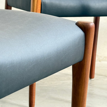 Close-up of two Fully Restored Fler 64 Dining Chairs in liquorice vinyl with rounded wooden legs, set against a neutral background, highlighting their sleek mid-century modern design and refined material texture. Set includes 6 chairs.