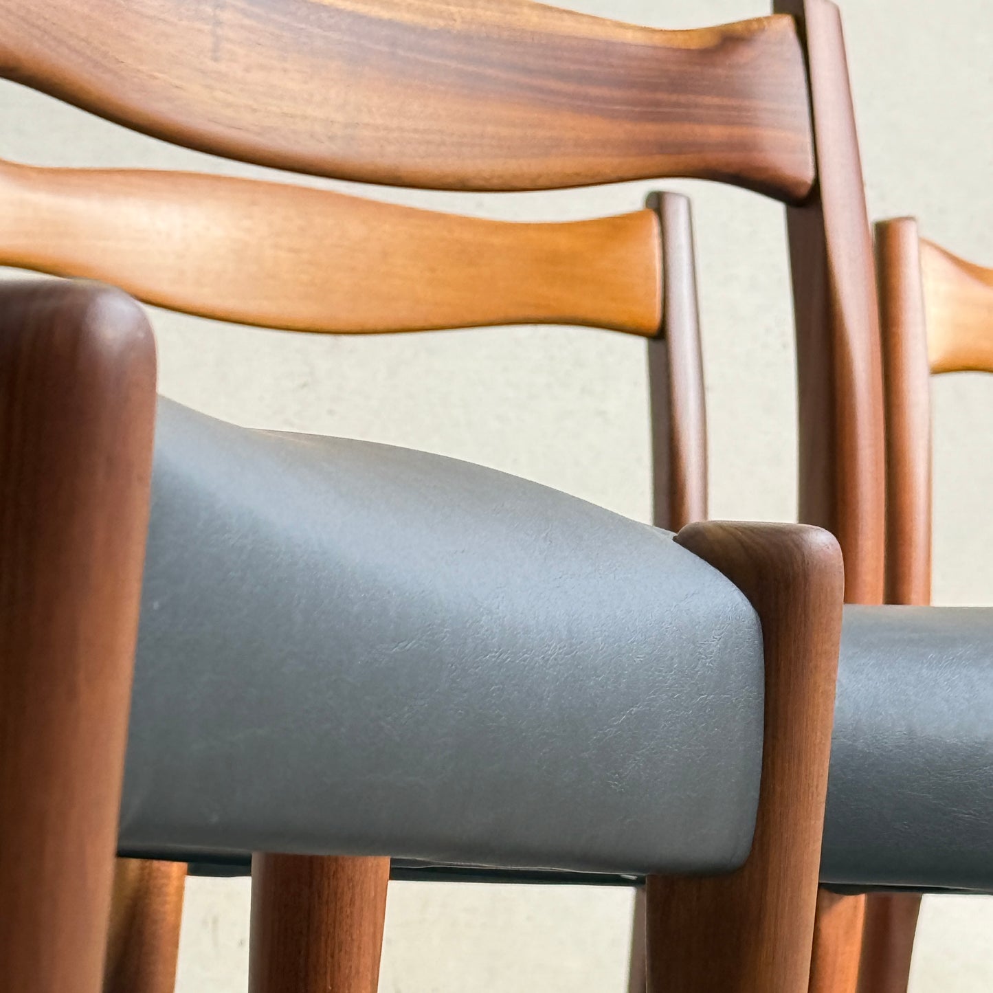 Close-up of three Fully Restored Fler 64 Dining Chairs in Liquorice Vinyl, arranged side by side against a light wall, highlighting their curved backrests and classic mid-century modern style.