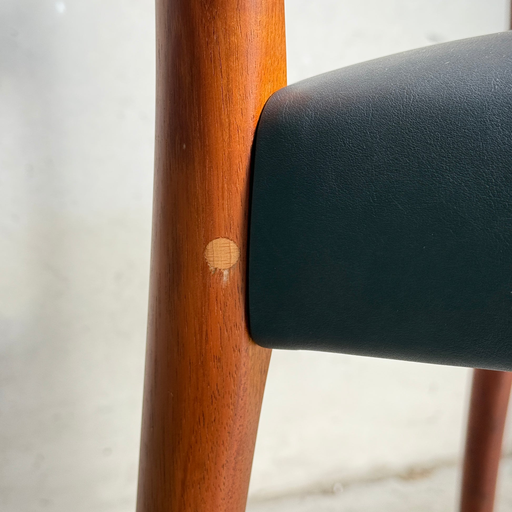 Close-up of a Fully Restored Fler 64 Dining Chair – Liquorice Vinyl from a set of 6, featuring a light blemish on the leg near the dark upholstered seat back, showcasing mid-century modern design against a softly blurred background.