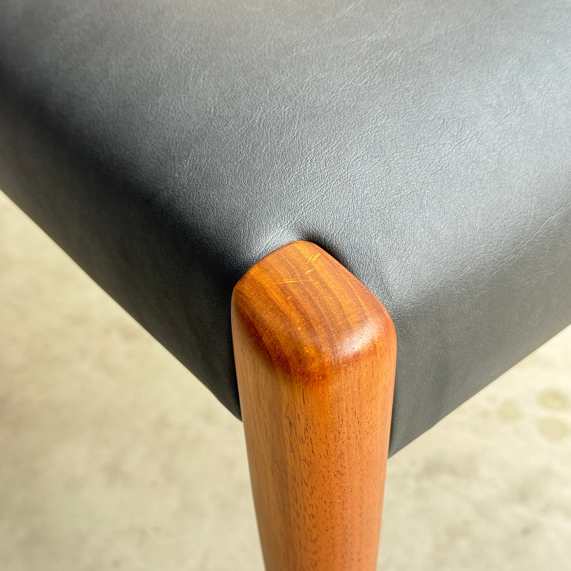 Close-up of a chair corner from the Fully Restored Mid-Century Parker 91 Oval Teak Dining Suite with 6 Fler 64 Blackwood Chairs, showing a smooth black seat and rounded wooden leg, highlighting texture and expert joinery.