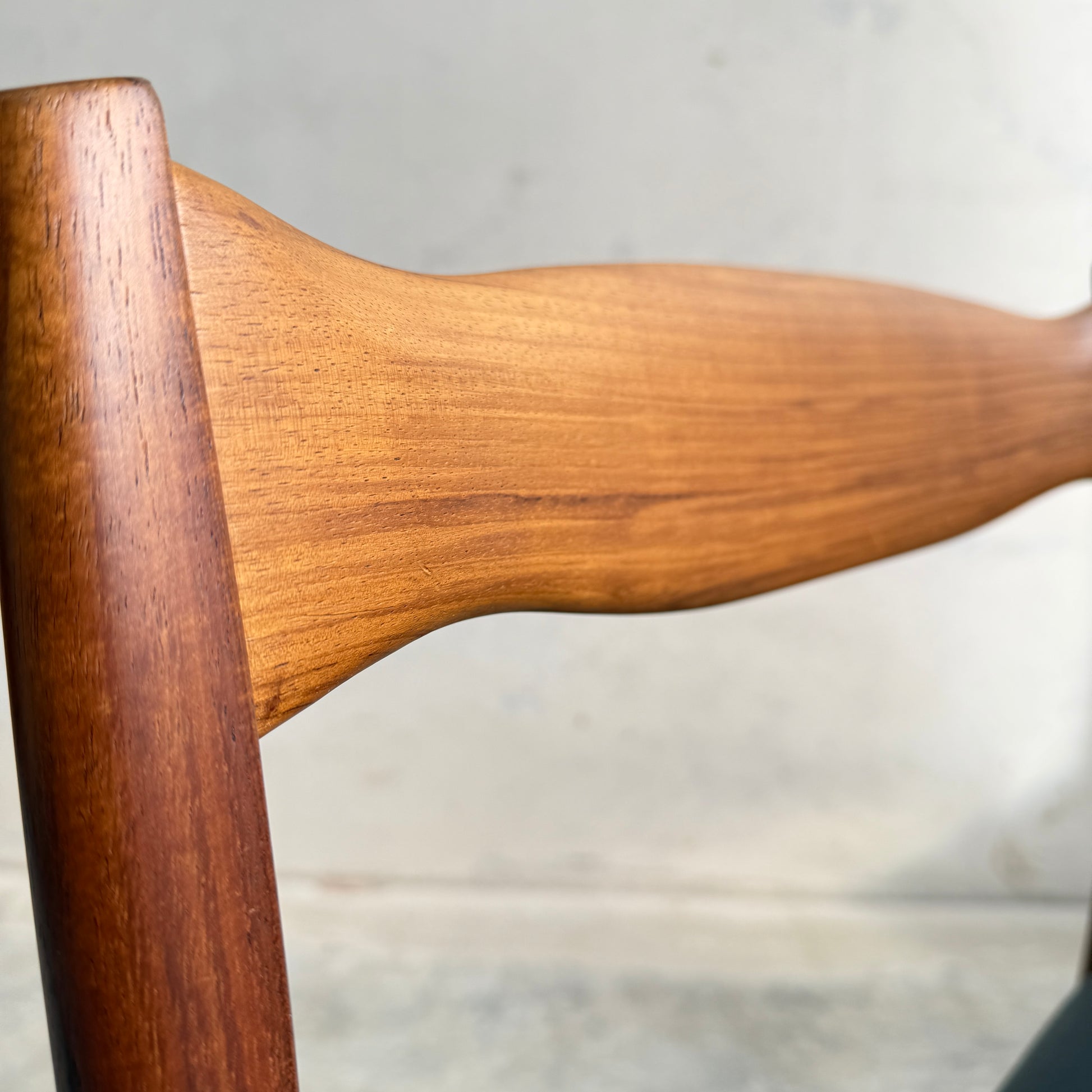 Close-up of the curved, polished wooden backrest of a Fler 64 Blackwood Chair from the Fully Restored Mid-Century Parker 91 Oval Teak Dining Suite, highlighting its smooth grain and modern design against a neutral background.