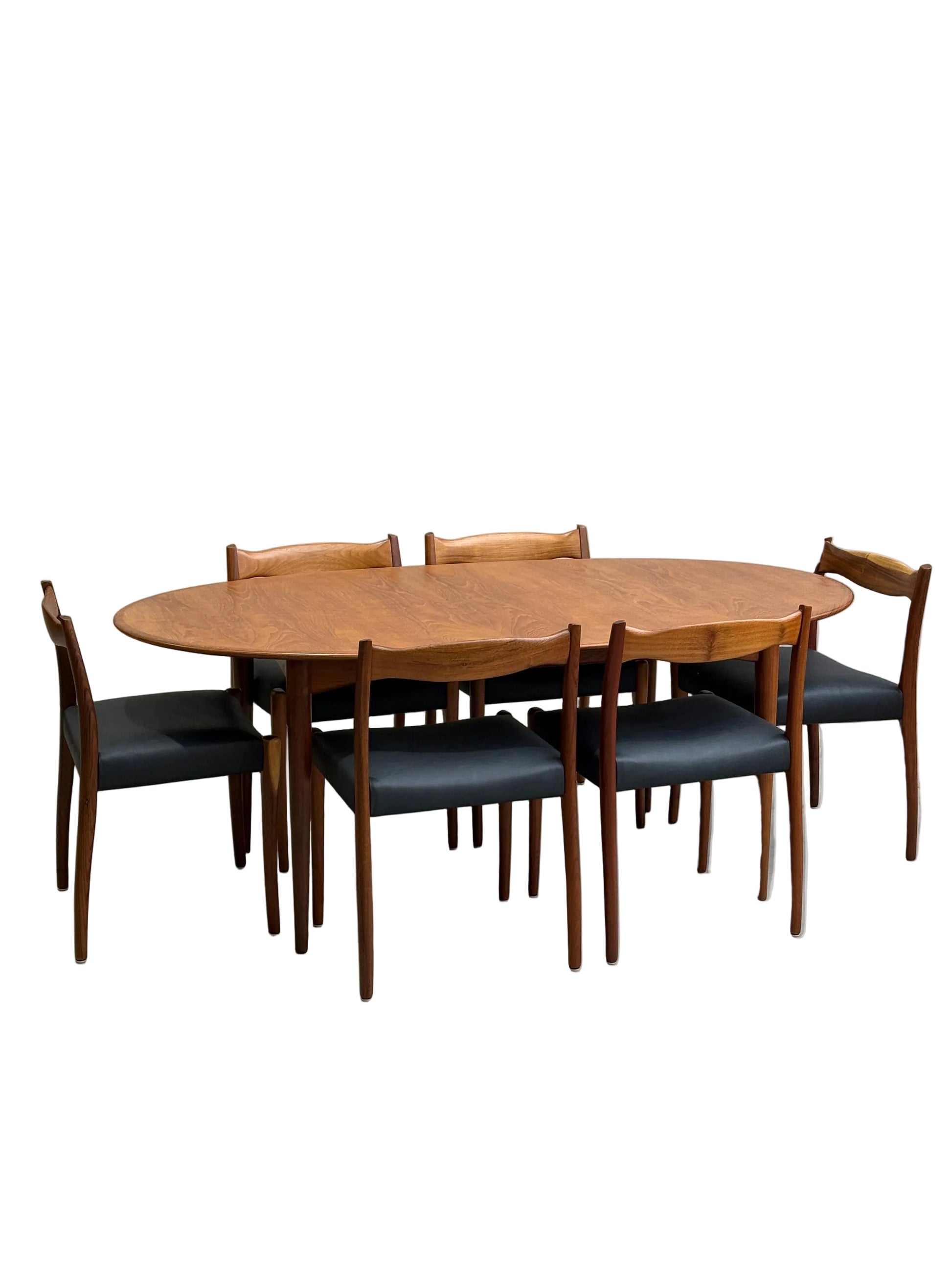 A fully restored mid-century Parker 91 oval teak dining suite with 6 Fler 64 blackwood chairs (Rediscover), set against a plain light gray concrete wall and floor.