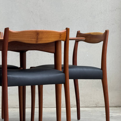 A fully restored mid-century Parker 91 oval teak dining suite with six Fler 64 blackwood chairs (Rediscover) sits against a plain, light-colored concrete wall for an authentic Australian dining space.